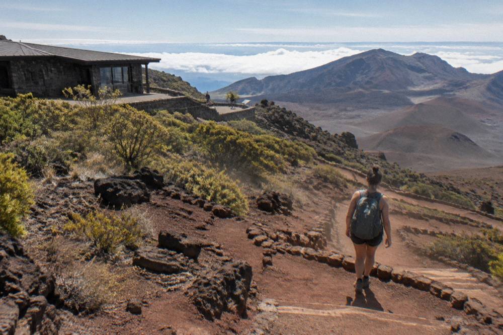 A hiker walking a cinder trail into the vast Haleakala crater under morning light
