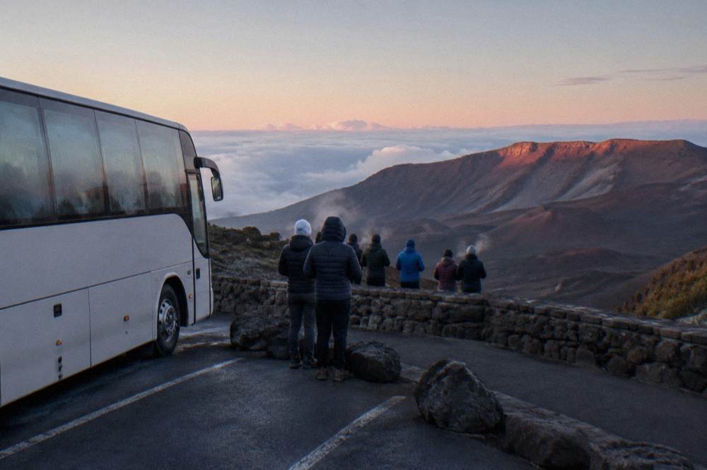 A guided coach parked near the Haleakala summit overlook at dawn with guests in warm jackets