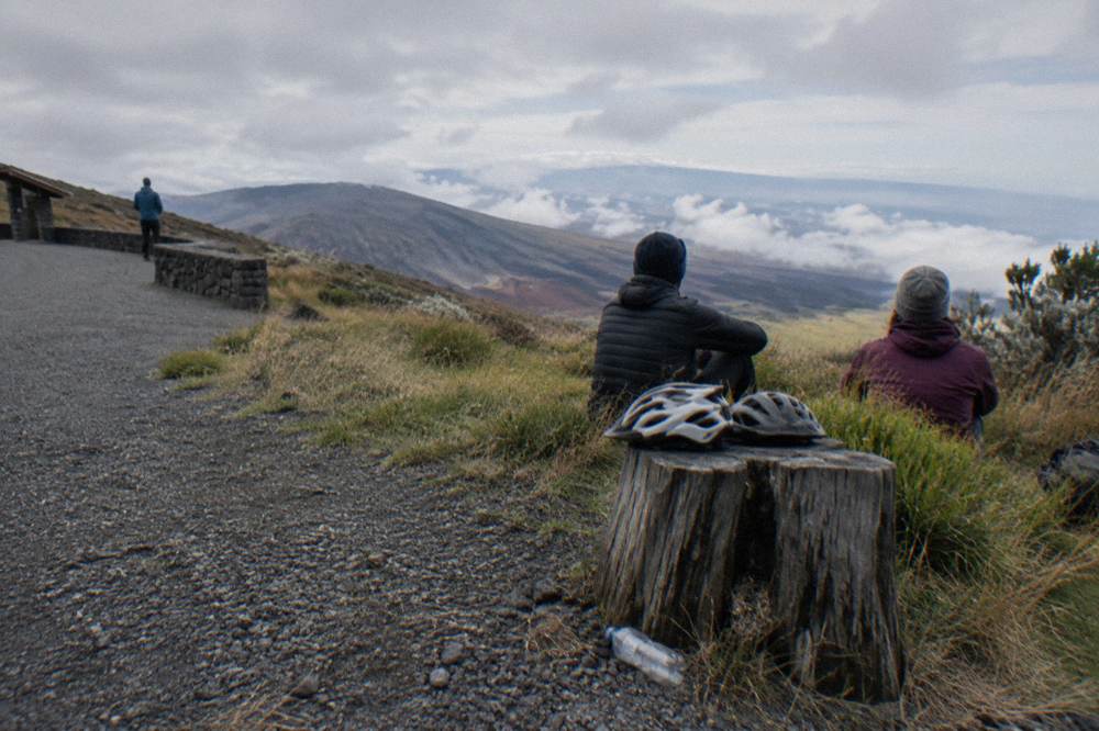 Riders in warm jackets resting beside parked bicycles at a pullout along the downhill road