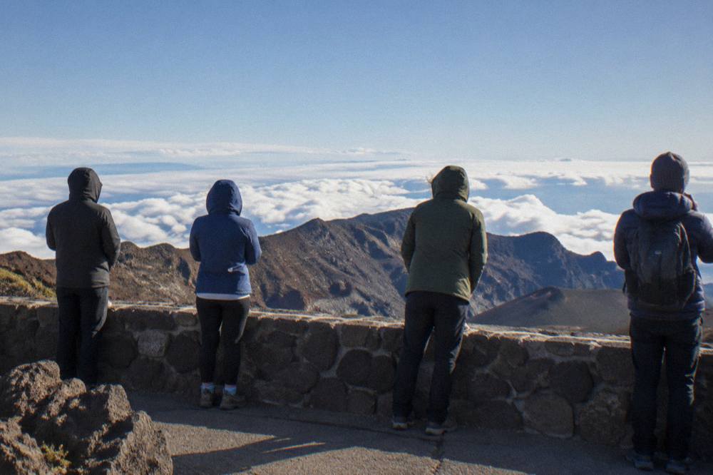 Warmly dressed visitors in jackets and hats standing at a stone overlook above the clouds