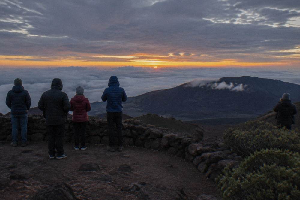 Small group of travelers in warm jackets standing at a high crater viewpoint