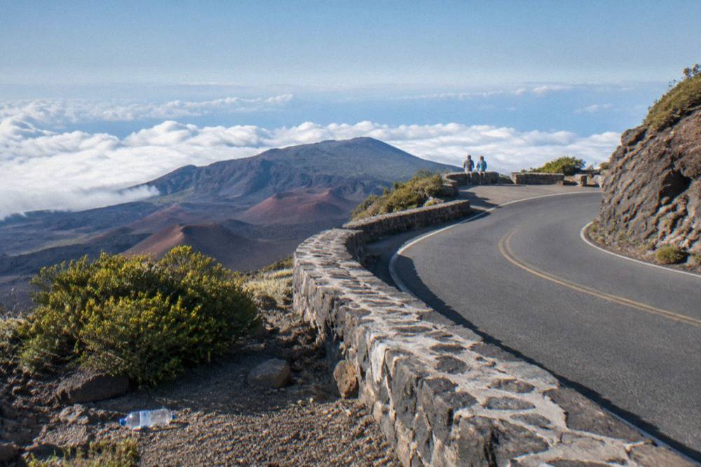 Rider on a bicycle descending a curving road above Maui's cloud line in morning light