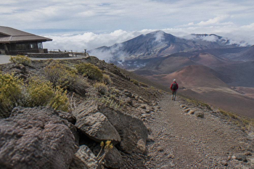Hiker on a cinder trail descending toward the layered walls of the Haleakala crater