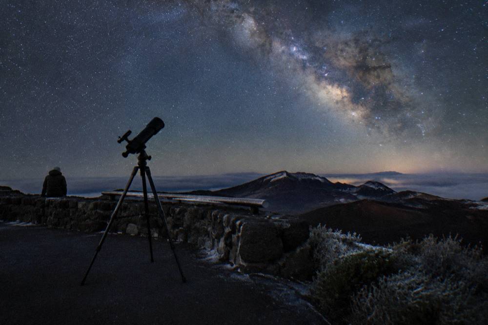 Telescope silhouetted against a starry sky at a mountain overlook