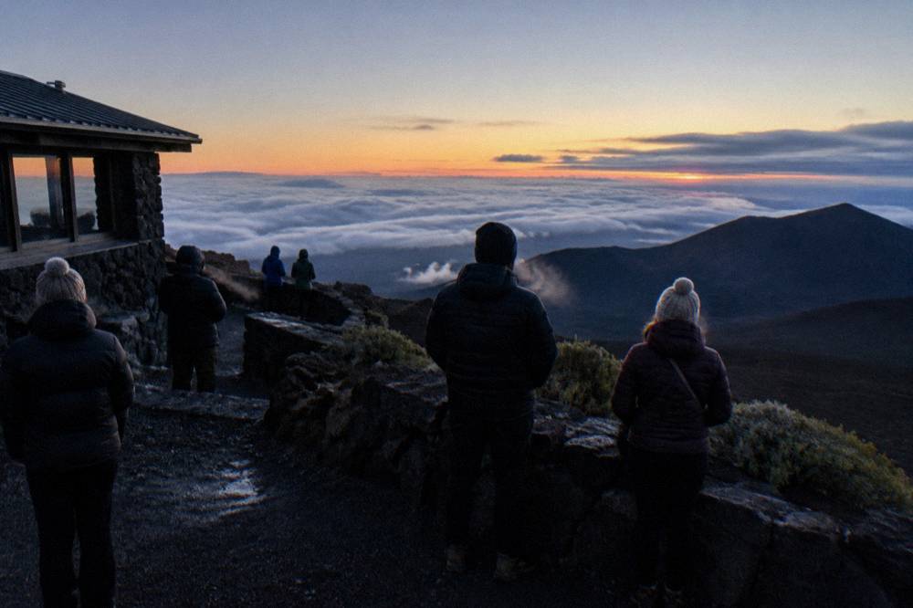 Warm layers on visitors standing at a summit overlook as evening light fades