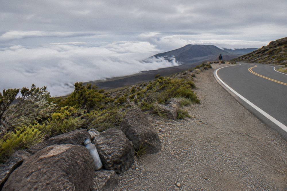 Two lane road curving along the open slope of Haleakala with cloud layers below