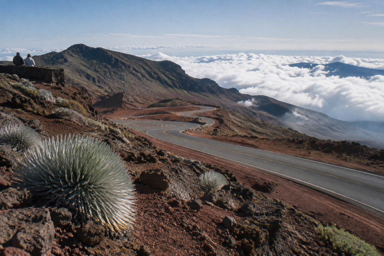 Winding paved road climbing the slopes of Haleakala volcano above a layer of clouds