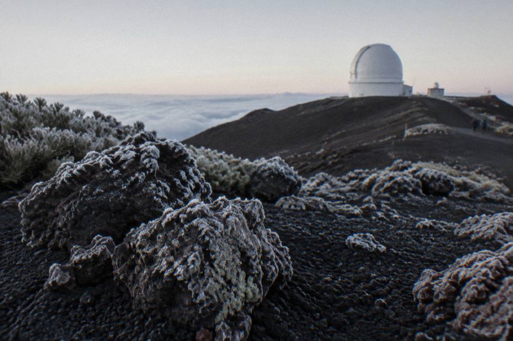 A rocky summit landscape at first light with frost on dark cinder and a pale horizon