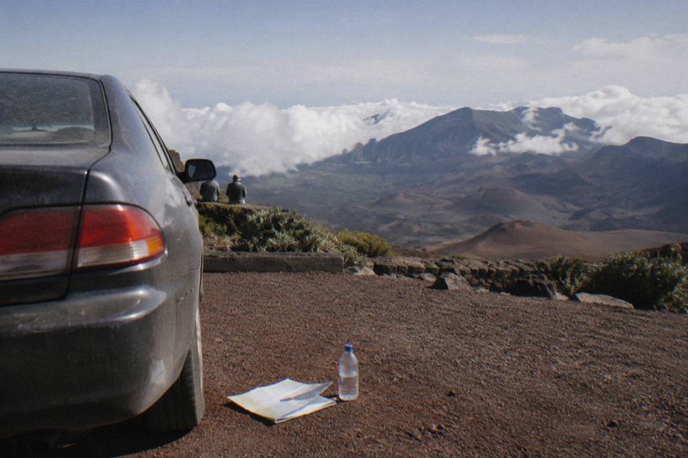 A parked car at a crater rim overlook under afternoon clouds