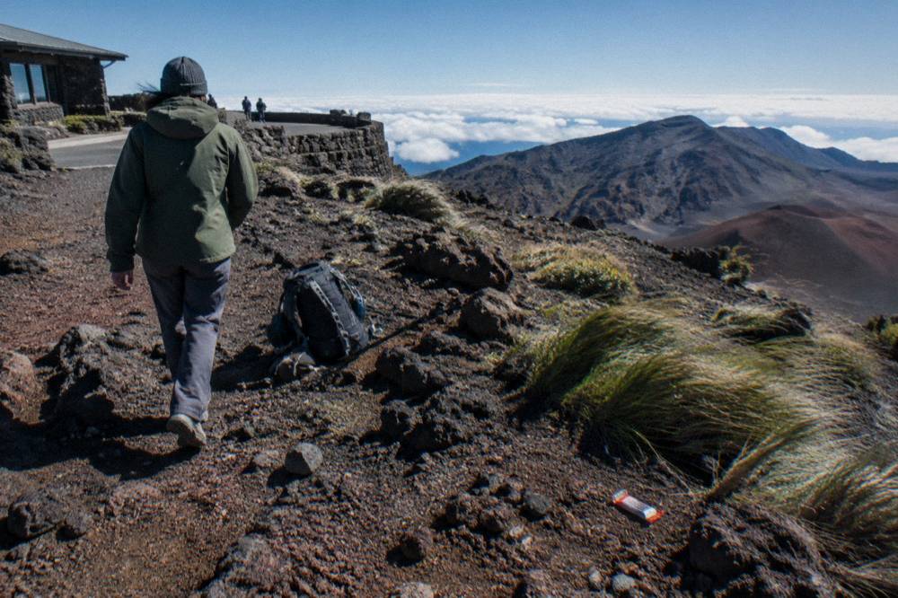 Jacketed rider walking a bicycle near volcanic rock at a high elevation stop
