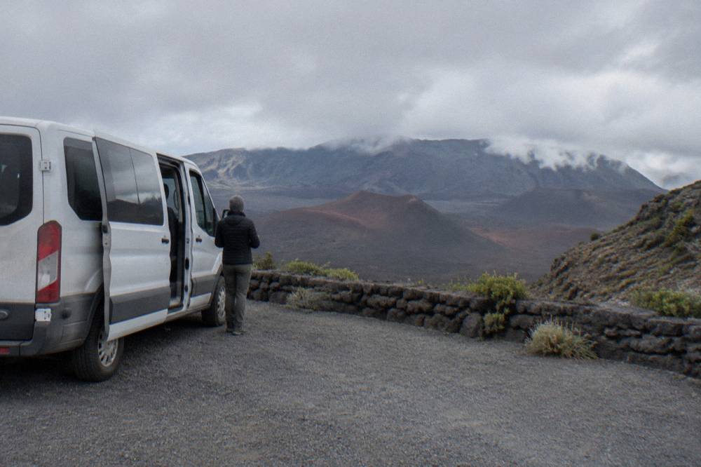 A tour van parked at a crater rim overlook with the basin stretching beyond