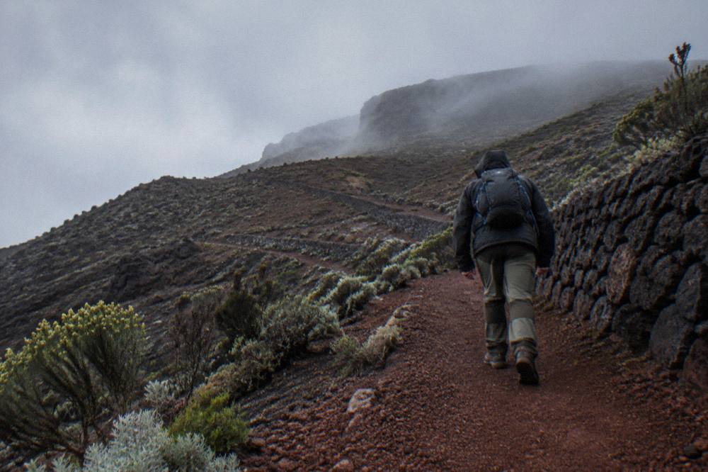 A hiker walking a switchback trail through red cinder slopes below the crater rim