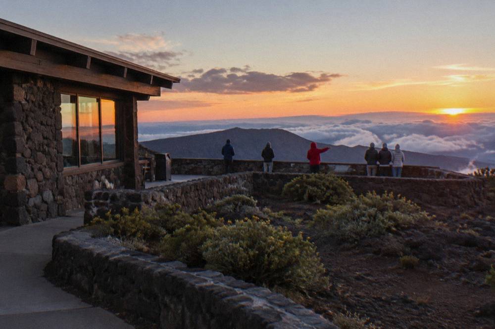 A small group of travellers watching the sunset from a rocky summit overlook