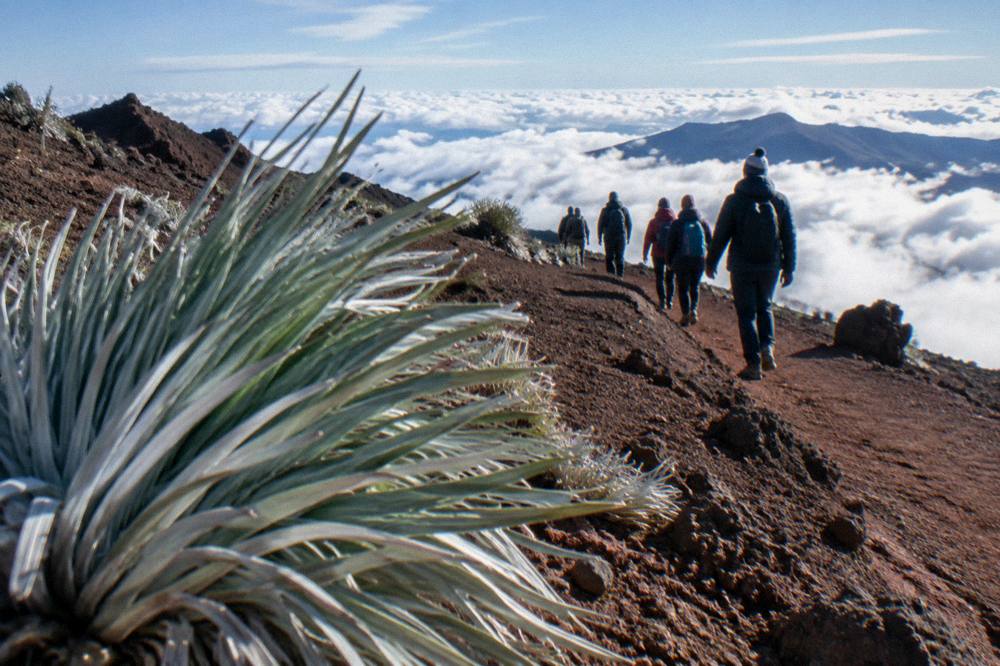 Hikers in warm jackets and hats walking the crater rim trail above the clouds