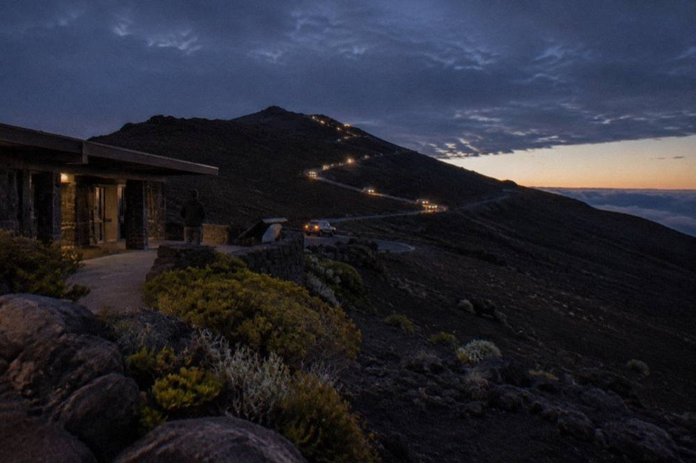 A line of headlights winding up the dark switchbacks of the Haleakala summit road before dawn