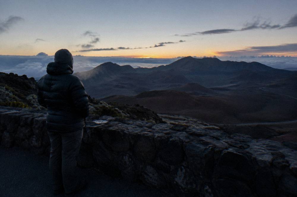 A bundled visitor in warm layers standing at a crater rim overlook in cold pre-dawn air