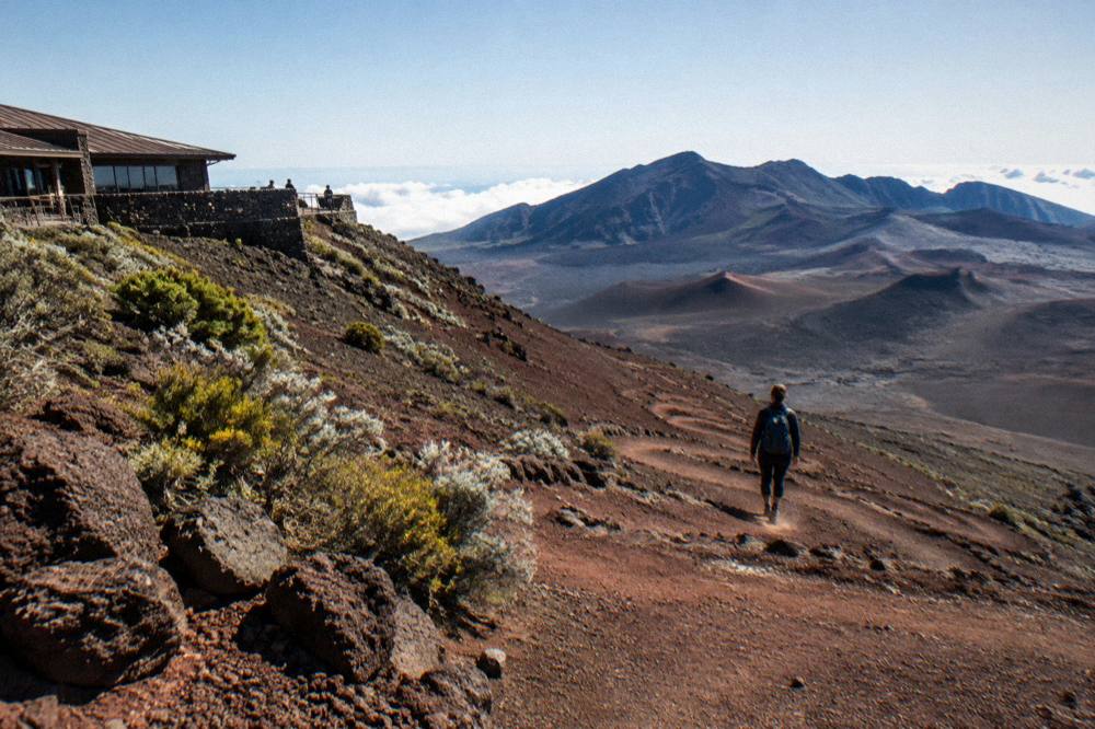 A hiker descending the red cinder slope of the Sliding Sands trail into the crater basin
