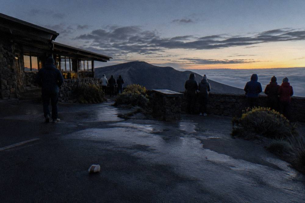 Visitors in winter jackets waiting at a summit overlook before first light