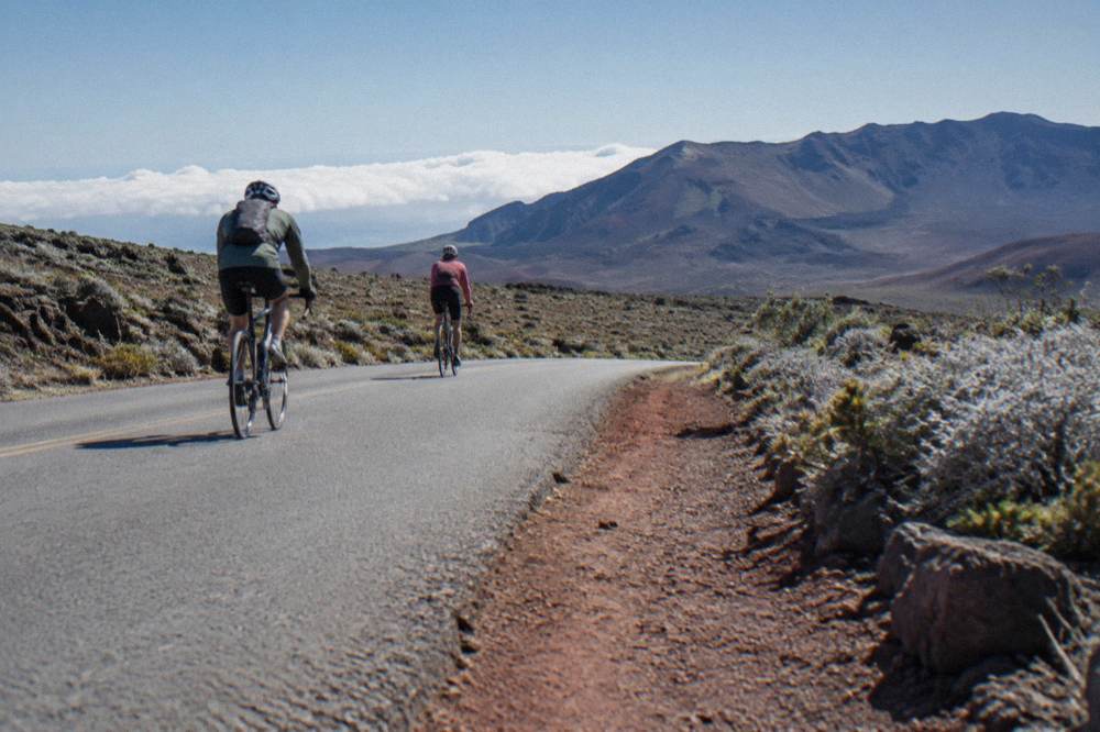 Cyclists descending the paved Haleakala crater road past dry shrubland