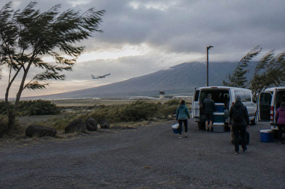 A gravel park and ride lot in Kahului with vans loading passengers at dawn