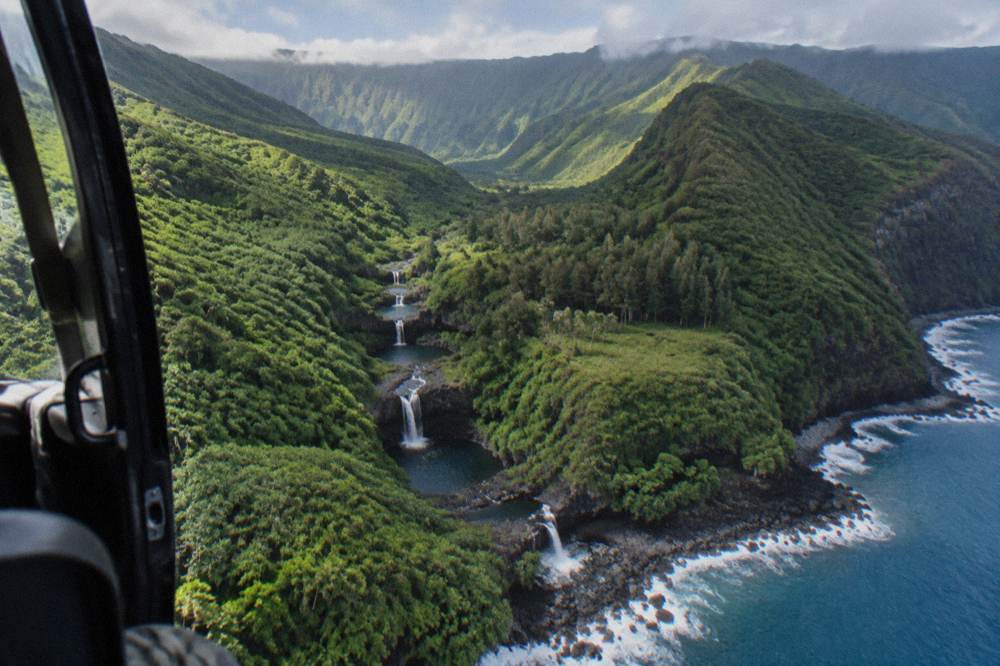 A helicopter flying above deep green rainforest valleys and a coastline
