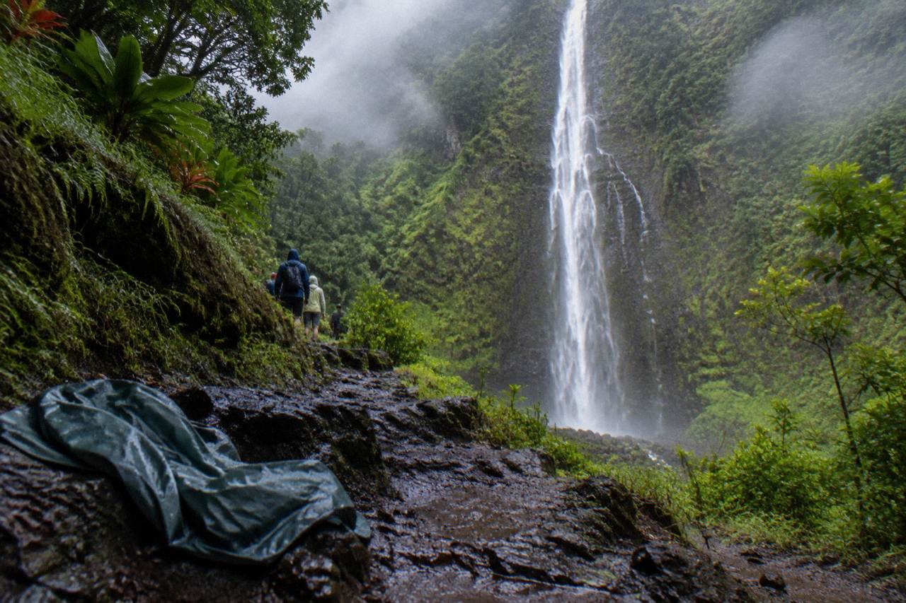 A tall waterfall pouring down a sheer cliff face at the end of a green rainforest valley