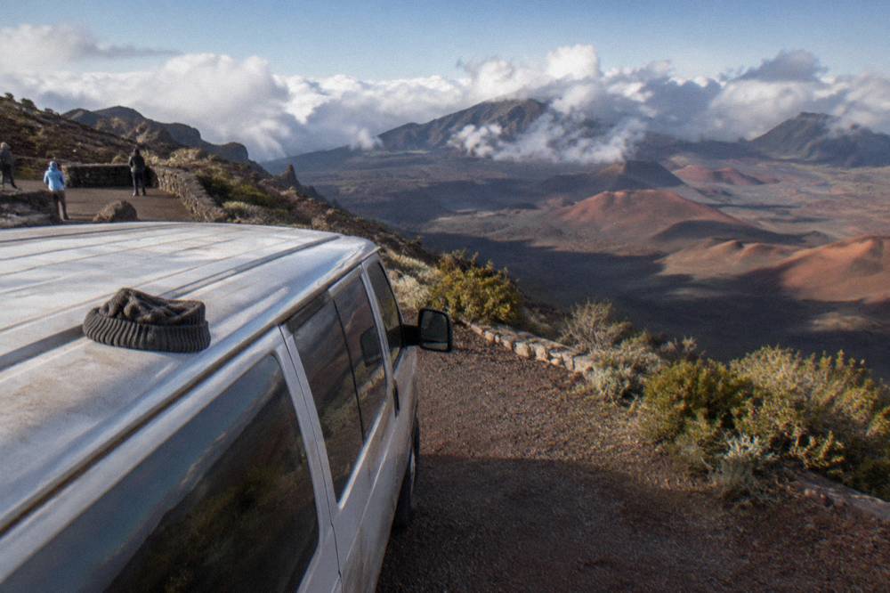 A small vehicle parked at a crater overlook with cinder cones beyond