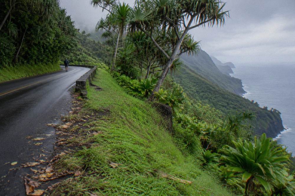 An open ridge road curving along a green valley slope toward the coast