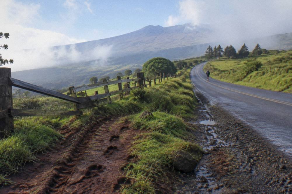 A long rural highway climbing through green pastureland toward a distant volcanic peak