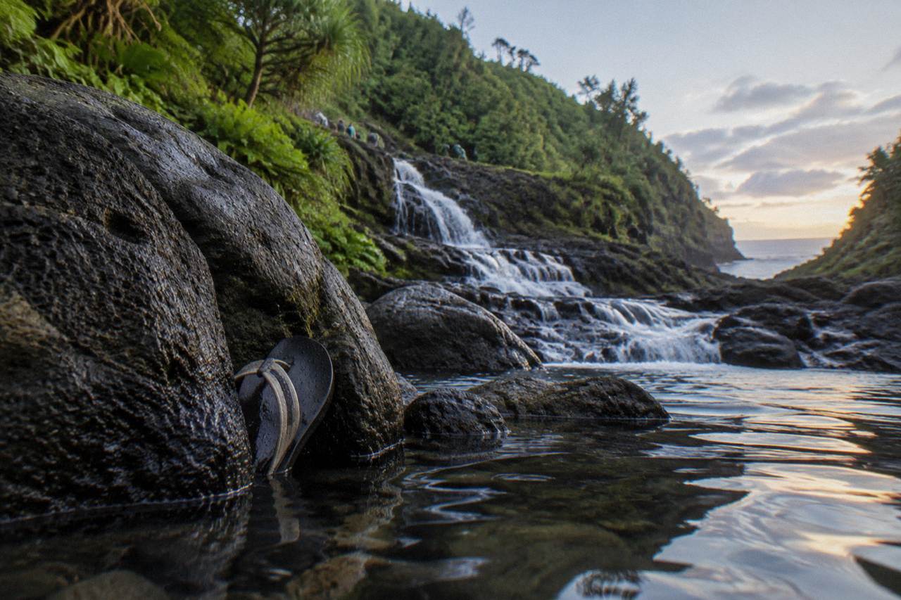 A series of terraced freshwater pools cascading down a dark lava rock gulch toward the ocean