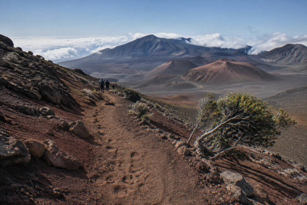 A narrow cinder footpath winding down red volcanic slopes toward distant cones inside a crater