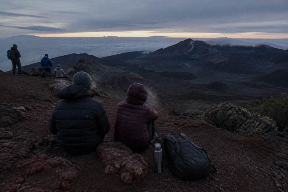 Hikers in warm layers resting on a cinder slope inside a large volcanic crater
