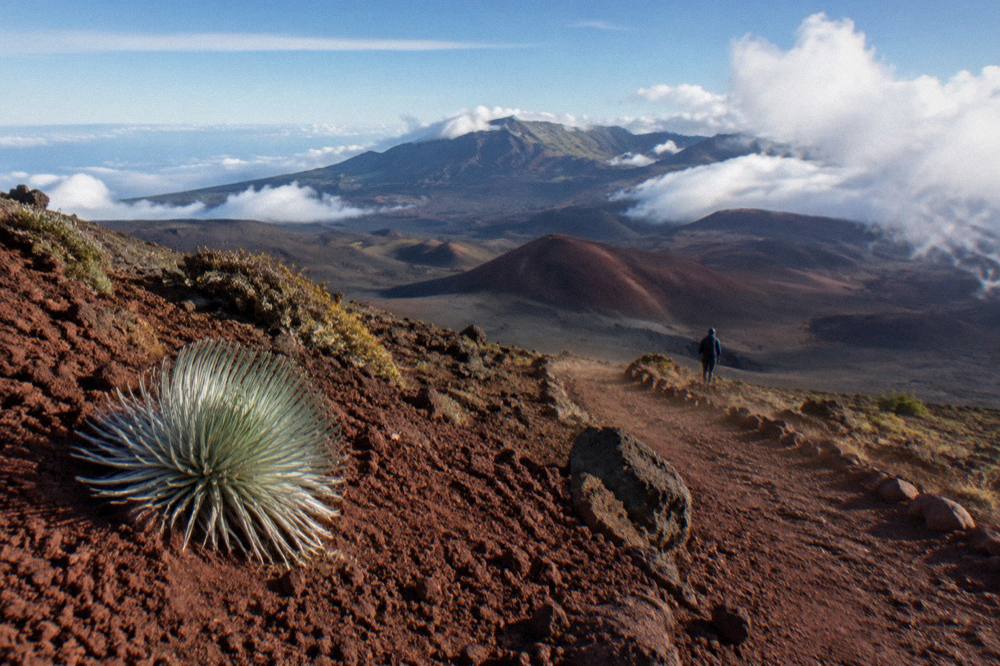 A wide volcanic crater interior with multiple cinder cones under scattered clouds