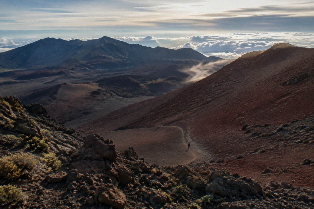 A cinder trail descending between red and gray slopes inside a volcanic crater under a wide sky
