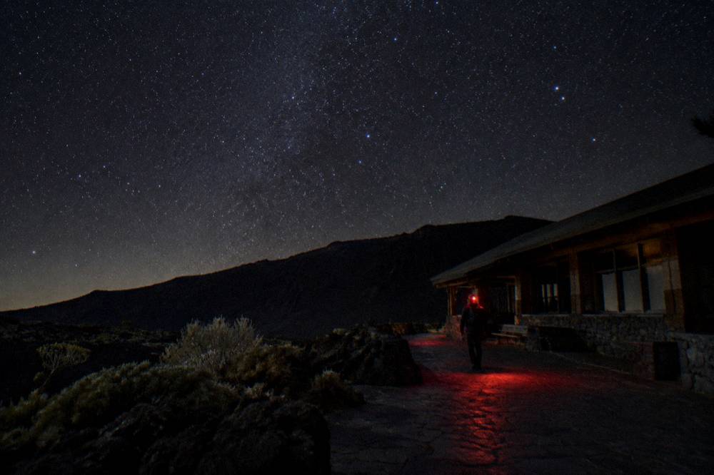 A dark night sky filled with stars above the silhouette of the crater rim
