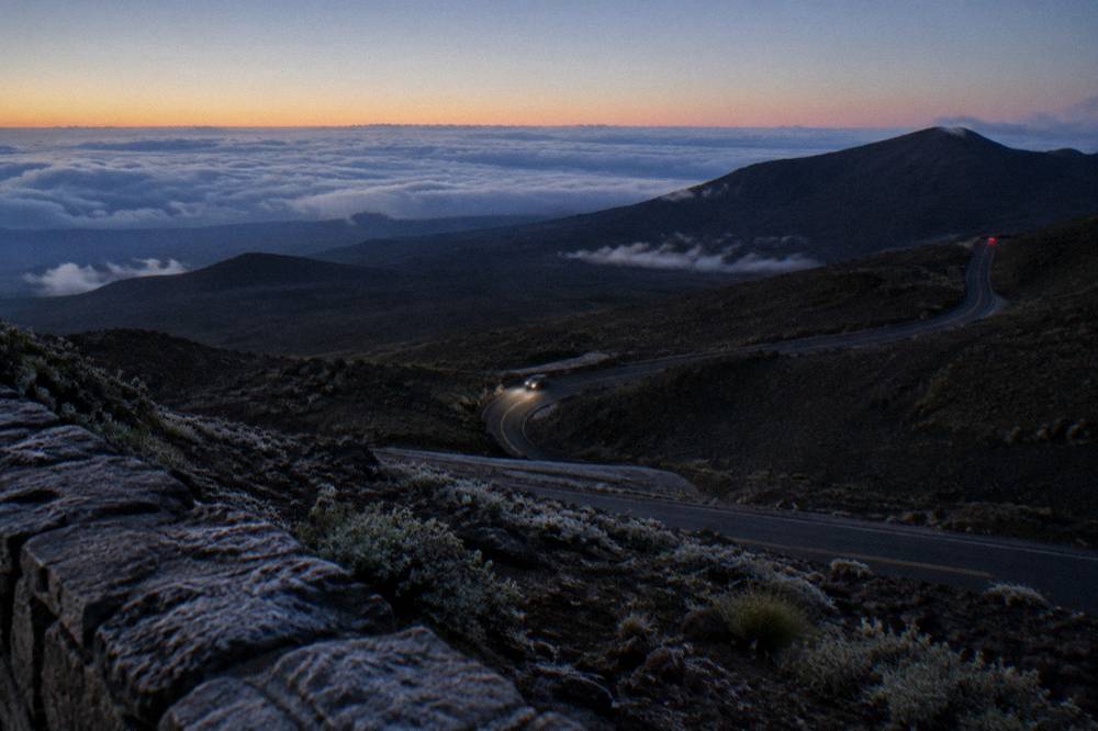 Dark mountain road winding uphill before dawn with headlights on the pavement